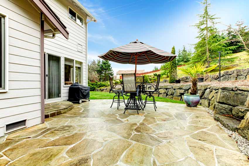 Flagstone patio with table, chairs, umbrella, shade, and house siding