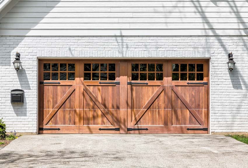 Garage with brick wall, lighting fixtures, driveway, and wood farmhouse garage doors