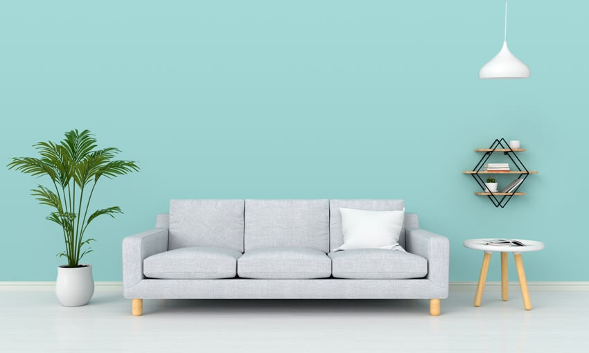 A gray sofa, potted plant and white hanging lamp in turquoise room