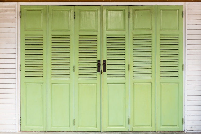 Green louvered garage doors with handles, and white wood siding