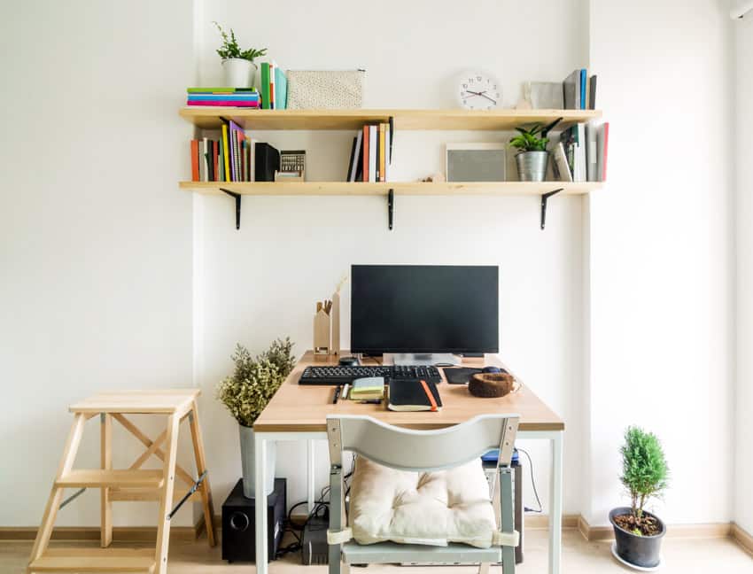 Home office area with shelves, desk, computer, chair, white walls, and indoor plant