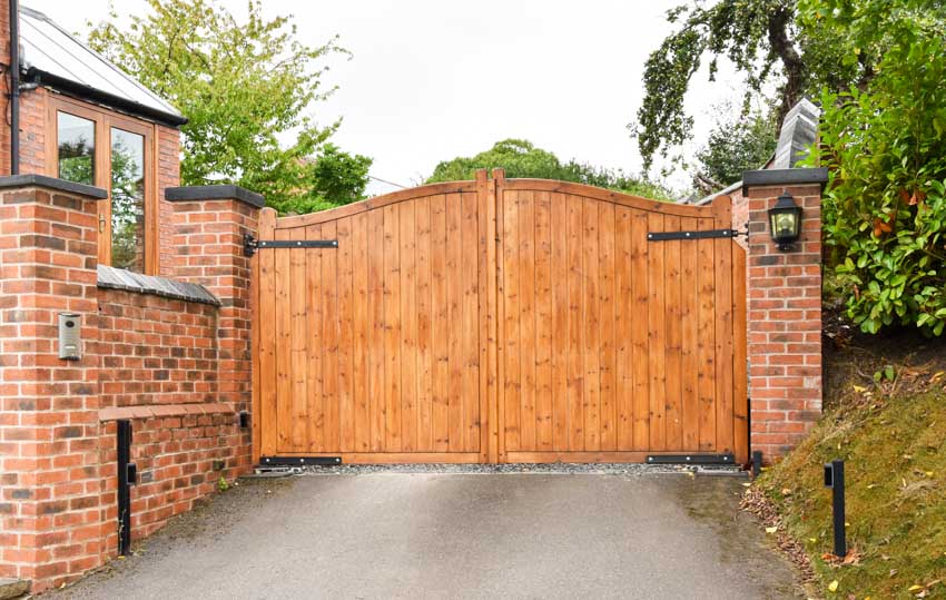 House driveway with wood swing gate, brick wall, and trees