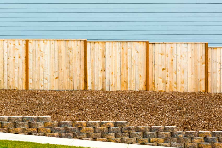 Privacy fence, raised stone foundation and blue siding