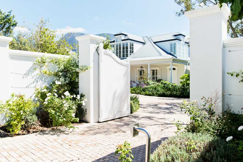 House exterior with white driveway swing gate, wall, and hedge plants