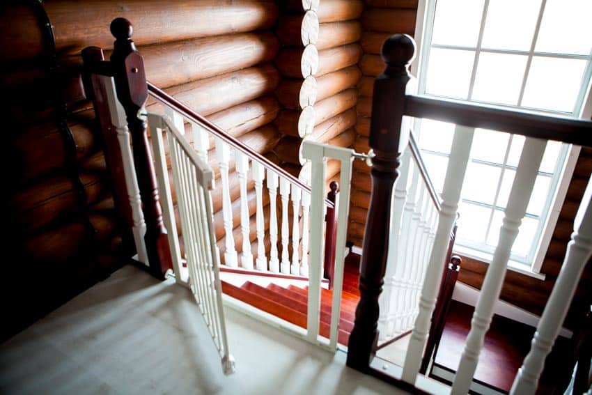 House interior with swing gate for stairs, railings, wood log wall, and windows