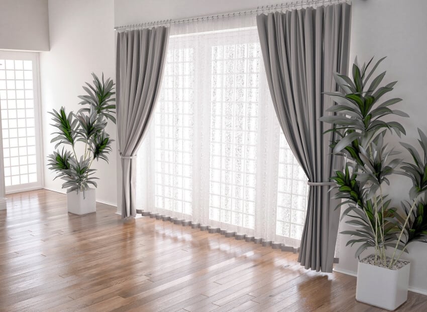 Interior of spacious room with sheer and dark gray curtains, potted plants and white walls