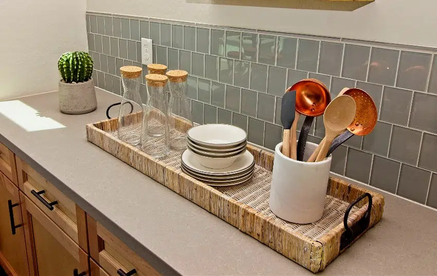 Kitchen counter with frosted glass backsplash and wicker basket with utensils, dishes, and glass decanters