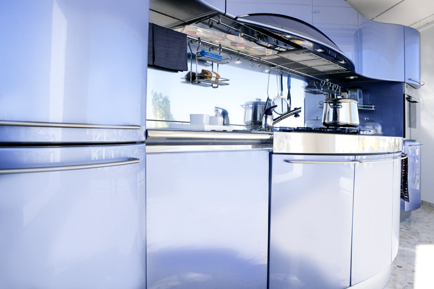 Kitchen with blue curved cabinets, backsplash, range hood, metal backsplash, and stove
