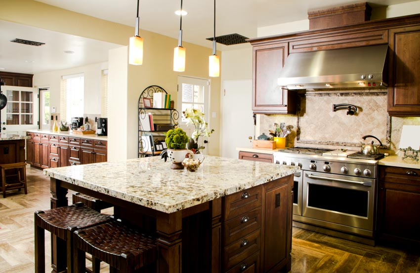 Kitchen with center island, chairs, limestone backsplash, wood cabinets, pendant lights, range hood, oven, and granite countertops