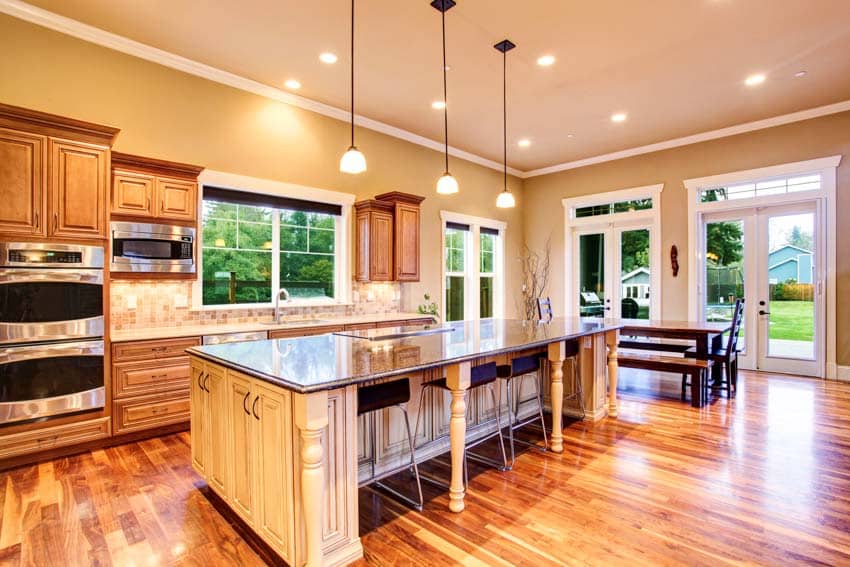 Kitchen with center island, countertops, pendant lights, cabinets, wood tile, backsplash, chairs, table, windows, and wooden flooring