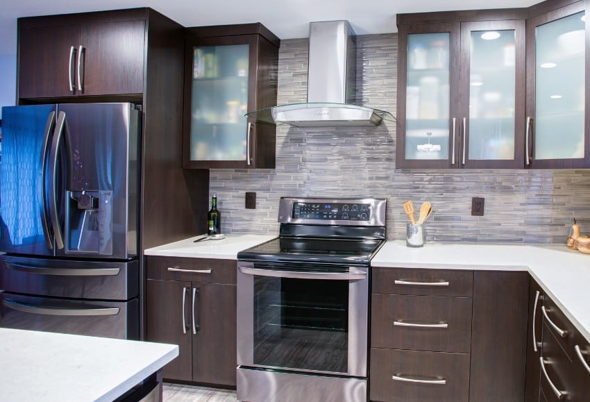 Kitchen with dark brown cabinets, fridge, stove with oven and range hood and frosted glass tile backsplash