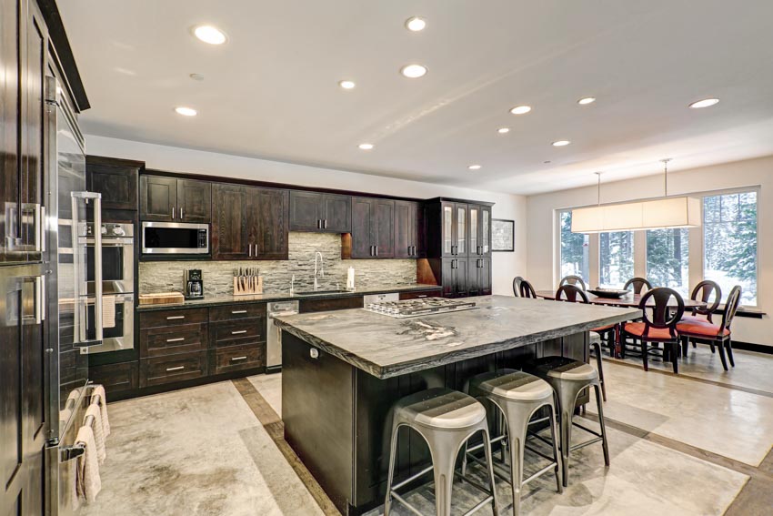 Kitchen with dark granite countertop, island, stools, tile floors, backsplash, wood cabinets, and ceiling lights