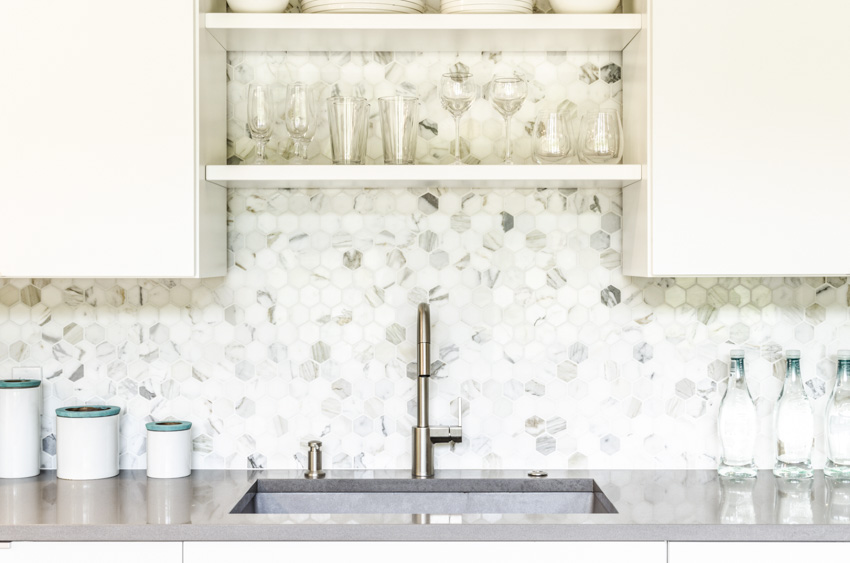 Kitchen with granite countertop, mosaic tile backsplash, sink, faucet, and shelf