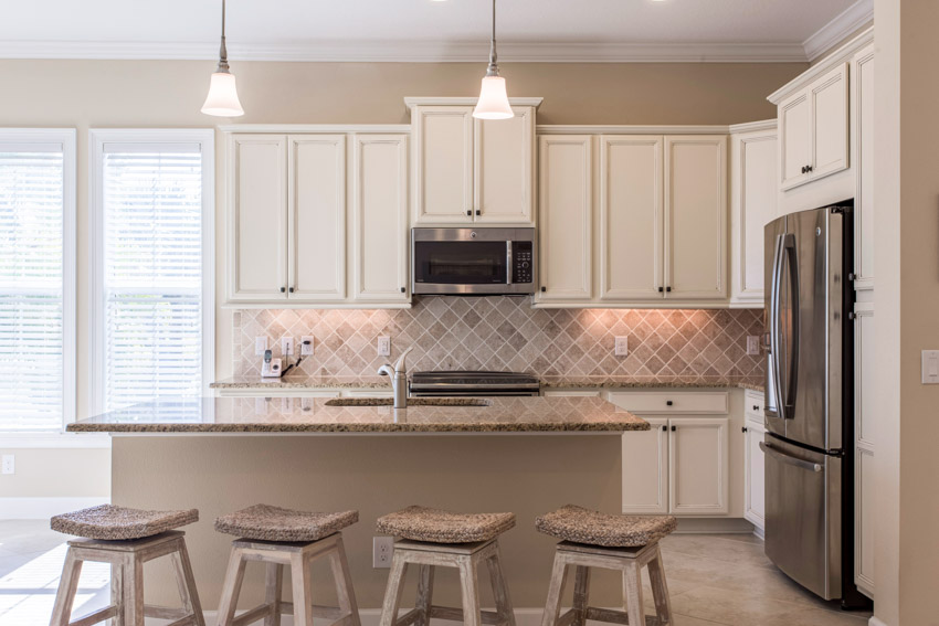 Kitchen with granite countertops, diamond tile backsplash, bar stools, pendant lights, and white cabinets