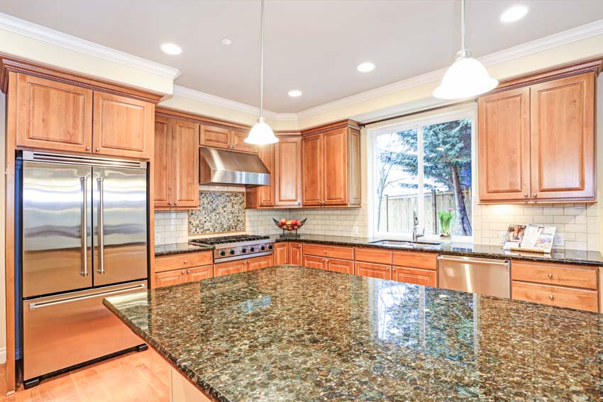 Kitchen with red oak cabinets, granite countertops, windows, hanging lights, gas oven, and subway tile