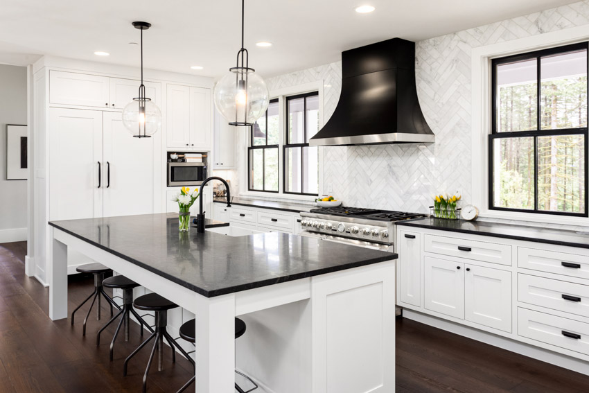 Kitchen with glazed porcelain with herringbone pattern, black countertops and range hood