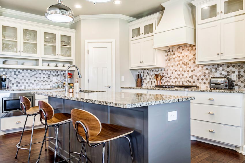 Kitchen with island, chairs, granite countertops, speckled backsplash, range hood, and white cabinets