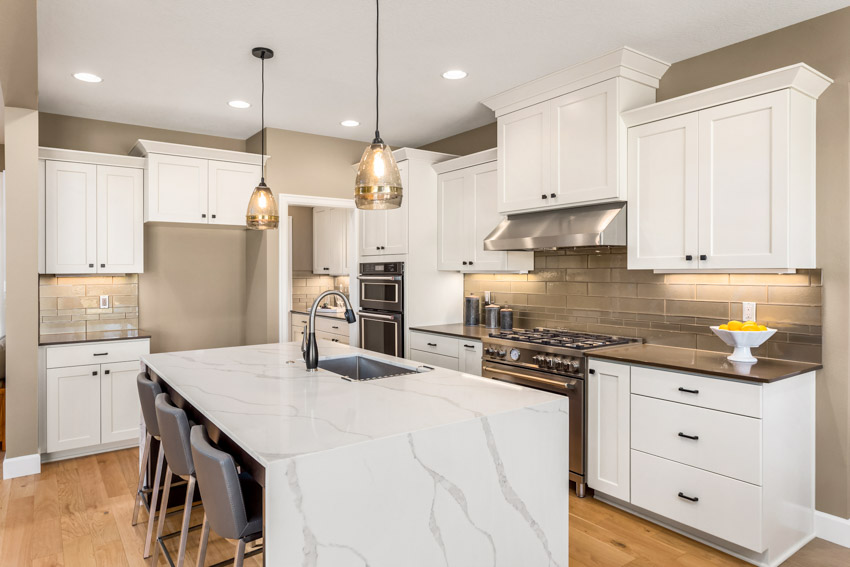 Kitchen with island, countertops, glass subway tile backsplash, white cabinets and chairs