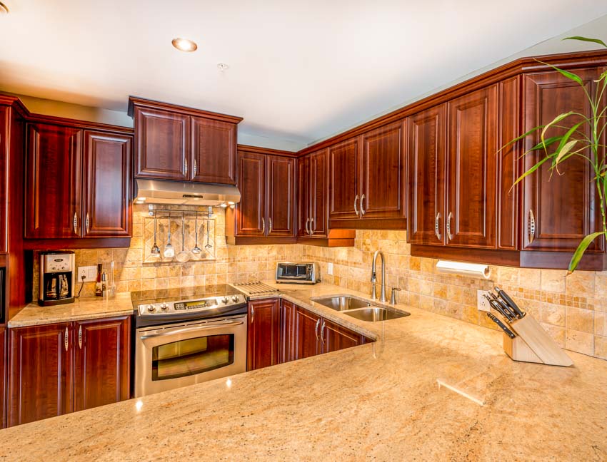 Kitchen with limestone tile backsplash, countertops, dark wood cabinets, range hood, sink, and faucet