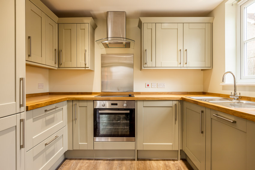 Kitchen with cabinets, oven, stove, backsplash, wooden countertop, sink, and window