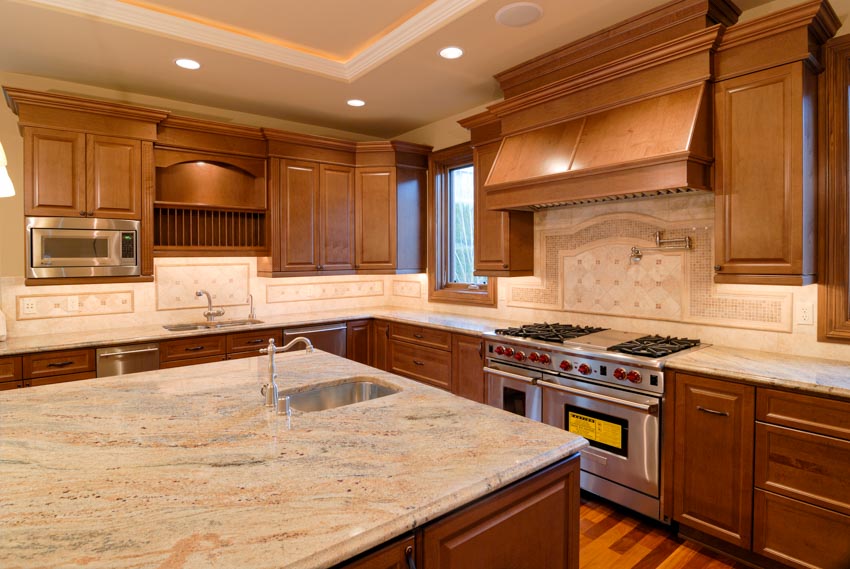 Kitchen with mosaic limestone backsplash, countertops, center island, sink, faucet, stove, range hood, and wood cabinets