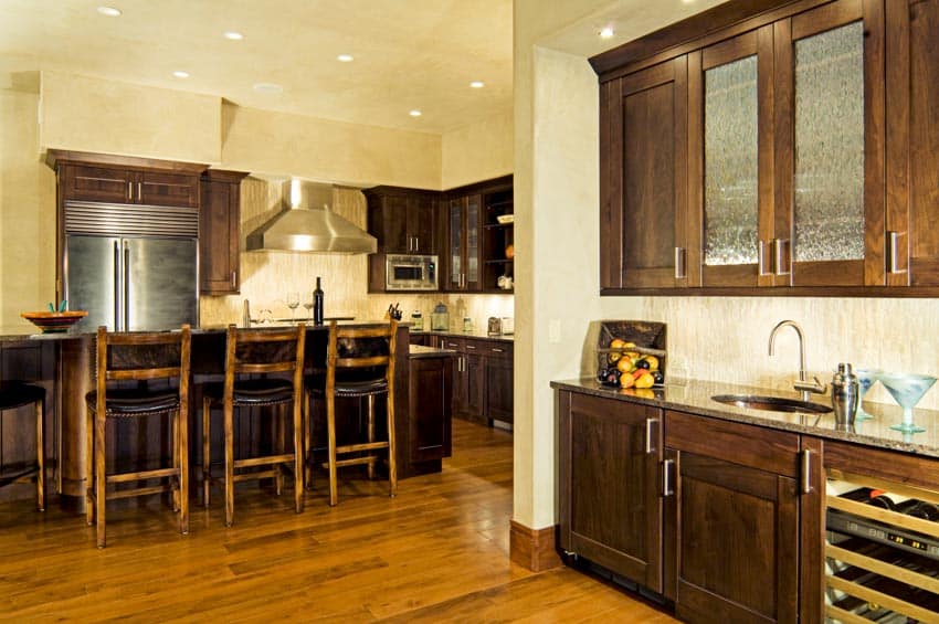 Kitchen with peninsula chairs wet built-in bar, cabinets, range hood, backsplash, and wood floors