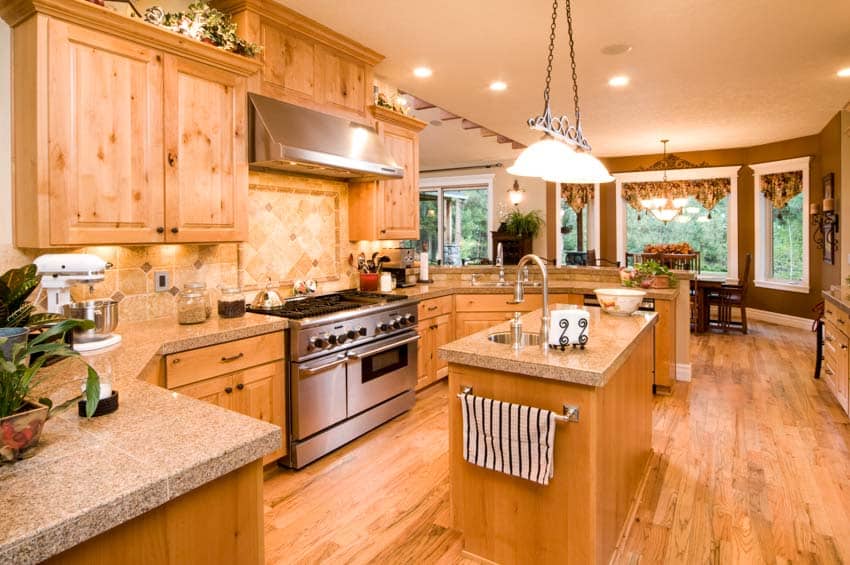 Kitchen with range hood, countertops, island, wood floors, windows, pendant lights, and hickory cabinets