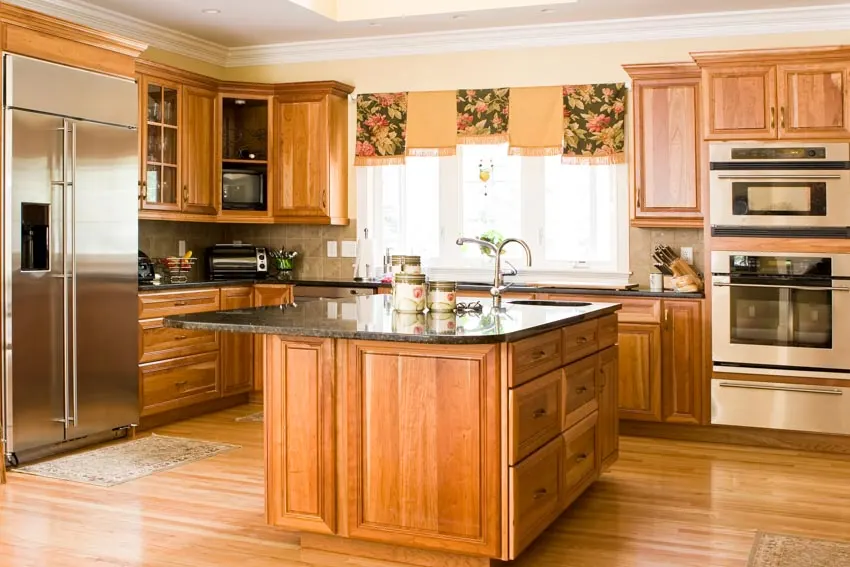 Kitchen with red oak cabinets, center island, countertops, windows, curtain, refrigerator, sink, and faucet