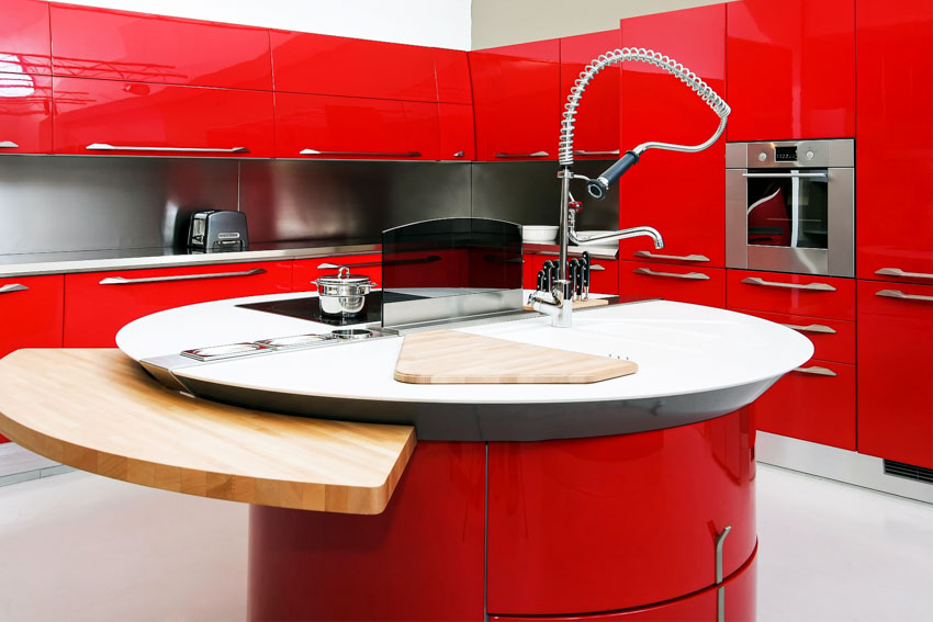 Kitchen with round island, red curved cabinets, sink, faucet, oven, and backsplash