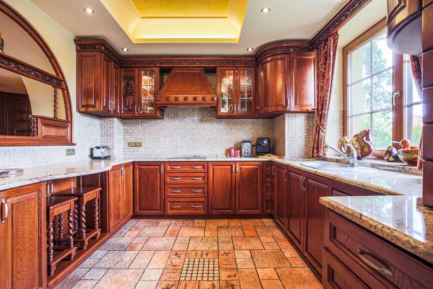 Kitchen with tile flooring, wood curved cabinets, countertops, backsplash, range hood, and windows