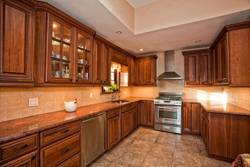 Kitchen with vein cut limestone backsplash, countertop, wood cabinets, tile floors, range hood, stove, and oven