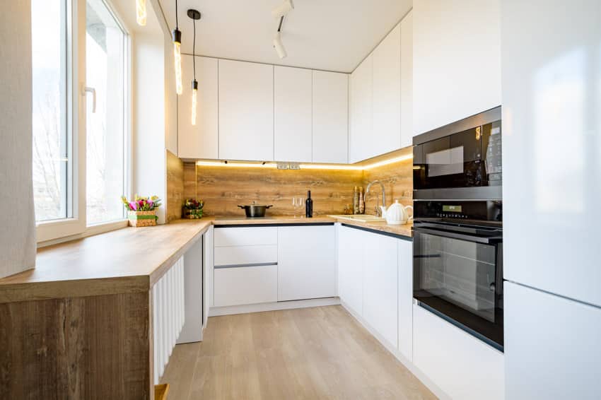 Kitchen with white frameless cabinet doors, wood backsplash, hanging lights, and windows