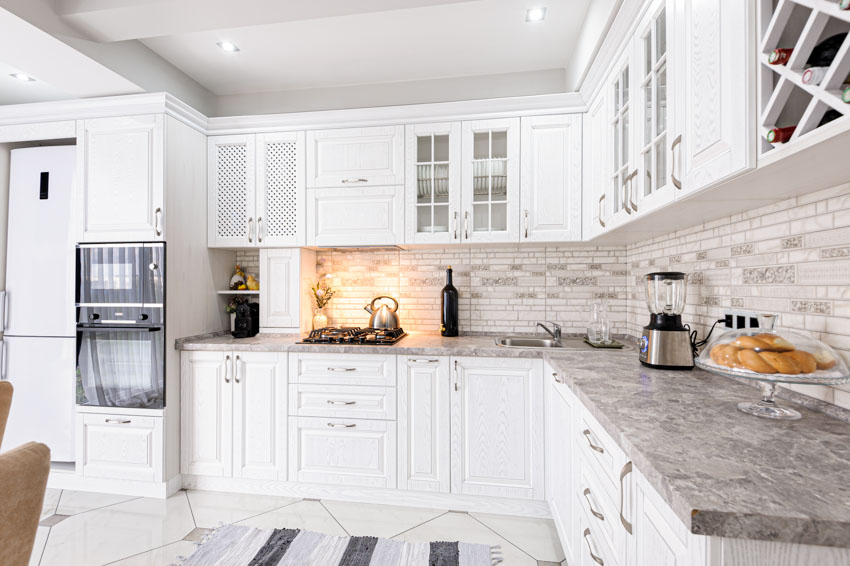 Kitchen with white matte cabinets, countertop, tile backsplash, oven, and under cabinet lights
