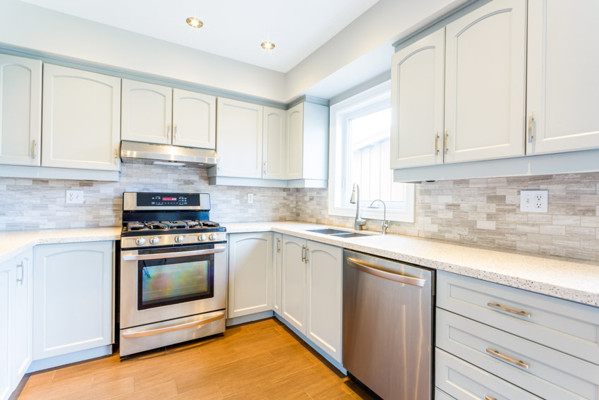 Kitchen with white cabinets, dishwasher, oven, tile backsplash, and windows