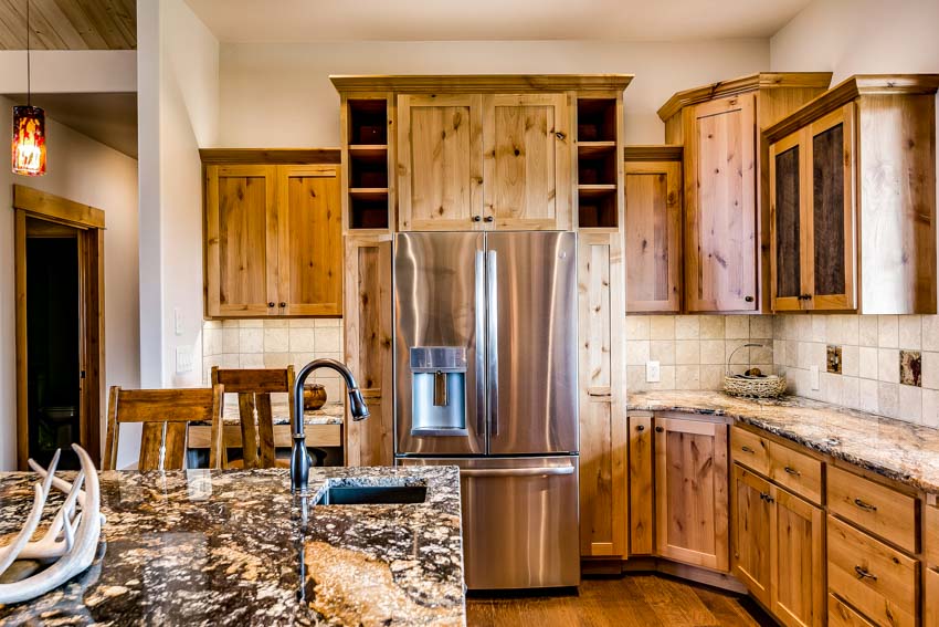 Kitchen with wood cabinets, limestone backsplash, countertop, sink, faucet, and refrigerator