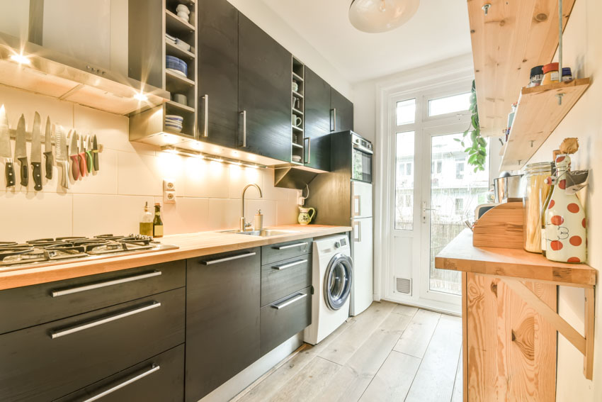 Kitchen with laundry machine, black cabinets, countertops, stove, and floating shelves