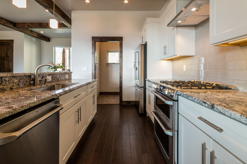 Kitchen with wood floors, granite countertops, cabinets, stove, tile backsplash, oven, stove, and range hood