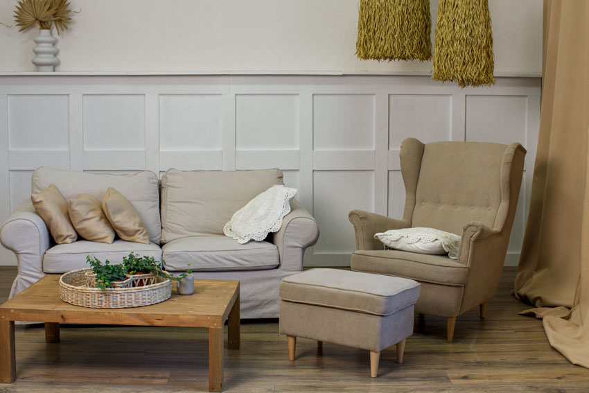 Living room with armchair, ottoman, coffee table, sofa, wainscoting, and wood floor