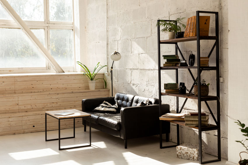 Living room with black leather couch, wood platform, lamp, coffee table, window, and freestanding shelf