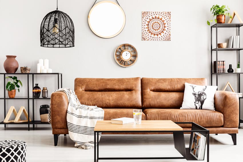 Living room with brown leather couch, coffee table, freestanding shelves, mirror, and pendant lights