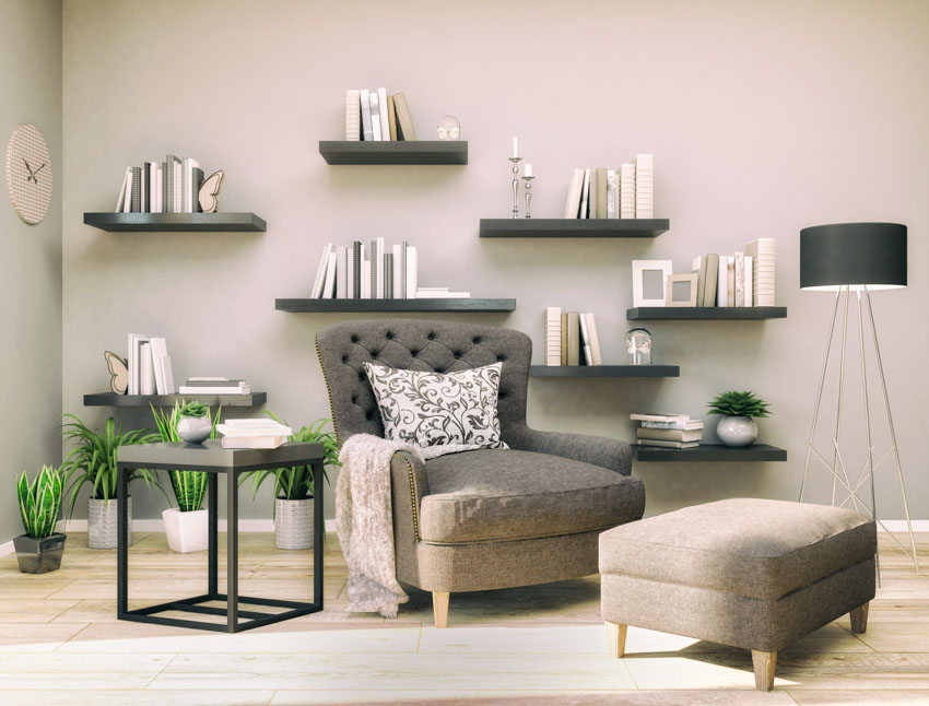 Living room with floating shelves, chair, ottoman, side table, wood floor, and lamp