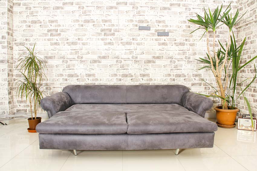 Living room with gray sofa bed, brick wall, and indoor plants