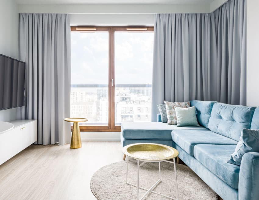 Living room with motorized curtains, glass door, blue couch, television, floating console table, and wood floors