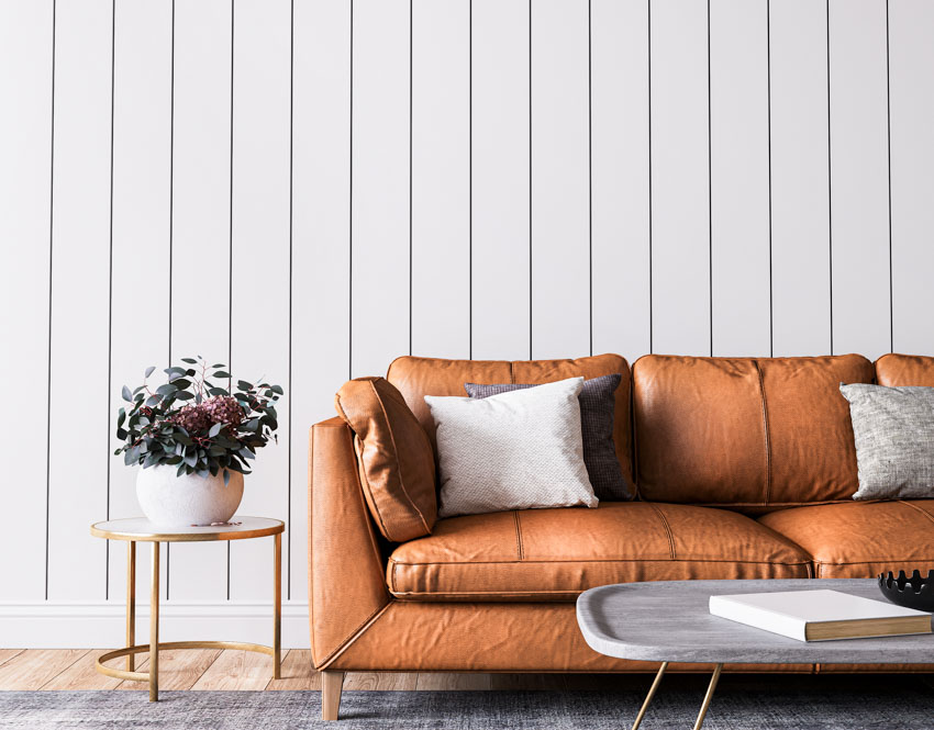 Living room with orange leather couch, pillows, vertical plank wall, side table, vase, flowers, and coffee table