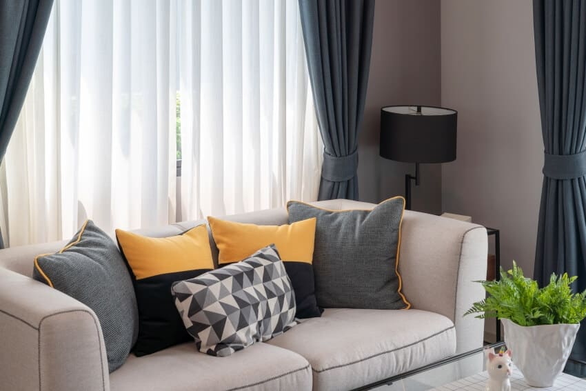 Decorated room with set of pillows on sofa and double curtains behind it