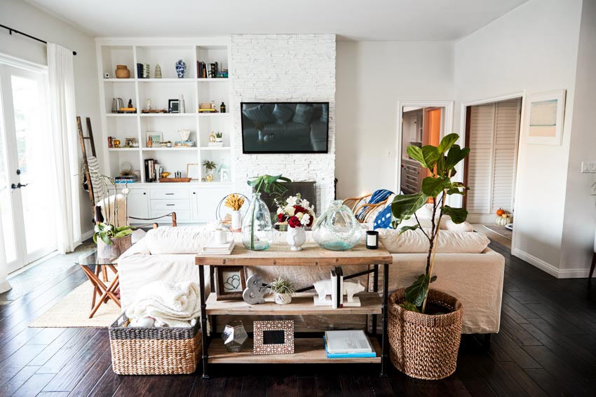 Living room with sofa table, indoor plant, wood floor, open shelves, laundry basket, and different decor pieces