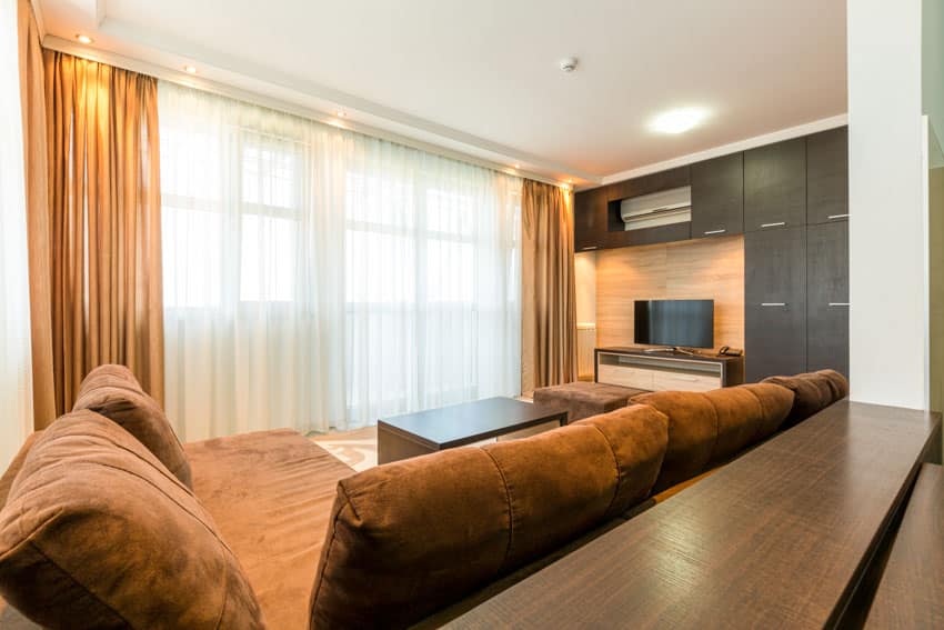 Living room with TV stand, television, cabinets, couch, pillows, and motorized curtains