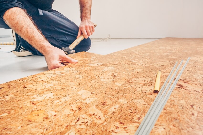 A man with hammer installing cork floor boards