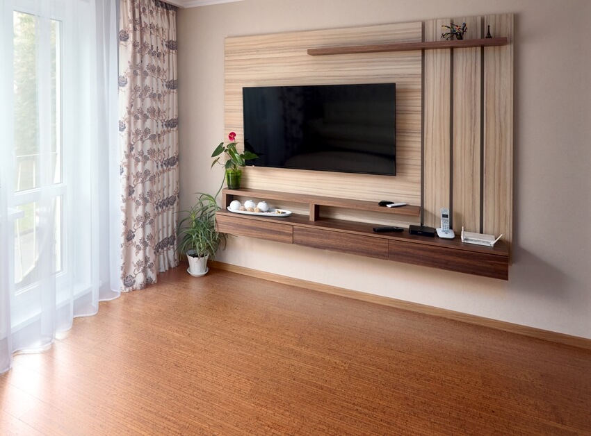 Minimalist living room with large tv over wooden cabinet, cork flooring and glass door to balcony