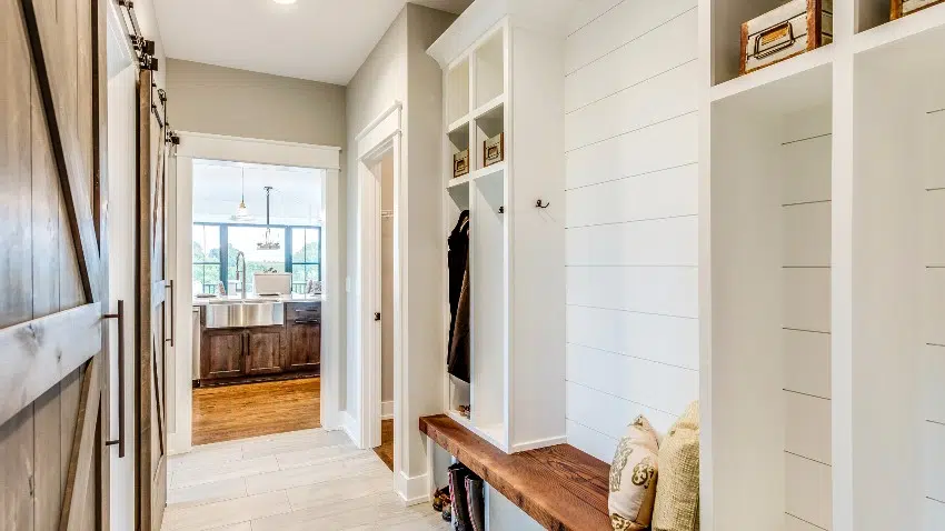 Mudroom with white walls, tile floors and natural wood bench with pillow